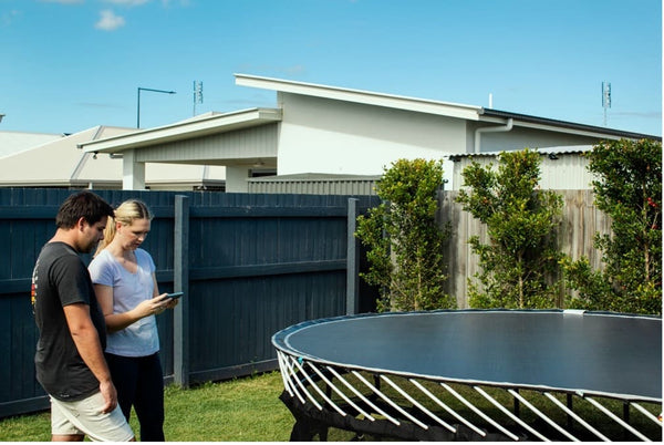 A man and a woman looking down at a phone next to a Springfree Trampoline without the enclosure.