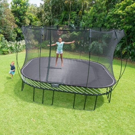 A girl jumping on a Springfree Square Trampoline while a little boy runs around it.