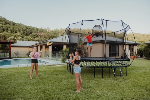A boy jumping on a Springfree Trampoline while two girls throw a ball outside of it.