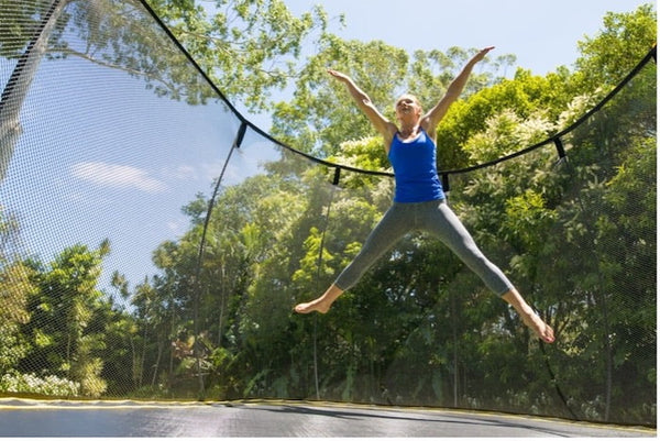 An athletic woman doing a Star Jump on a Springfree Trampoline.