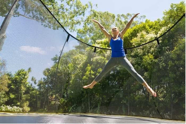 A woman doing a star jump on a trampoline.