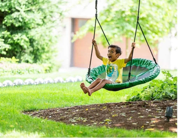 A child happily swinging on a green tree swing.