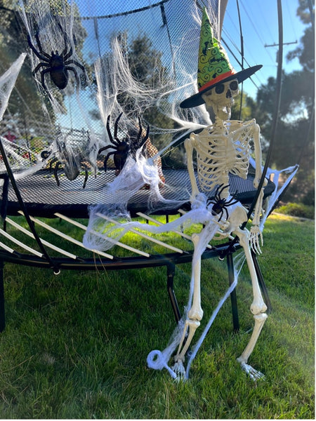 A Springfree Trampoline decorated with fake spiders and spider webs, with a skeleton standing next to it.