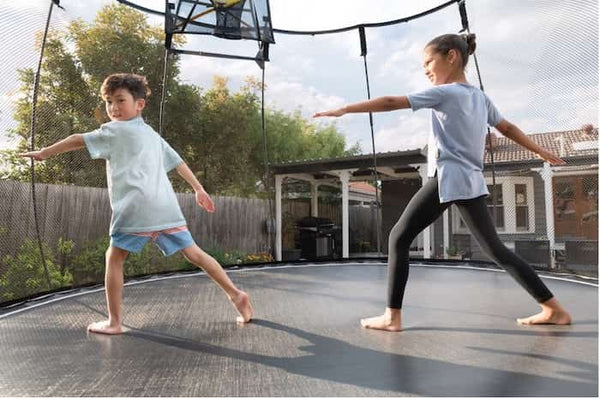 Two kids doing yoga poses on a Springfree Trampoline.