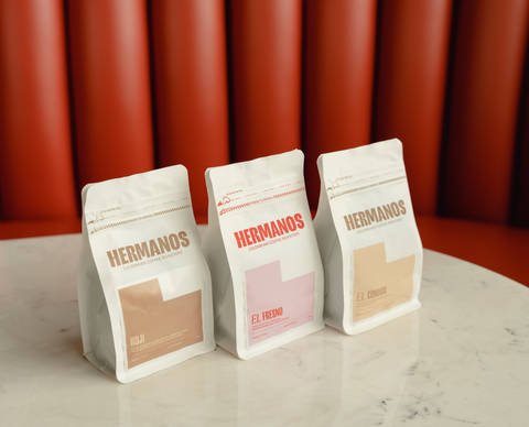 Three bags of Hermanos Colombian coffee roasters coffees, Koji, El Fresno and El Condor on a white table side by side