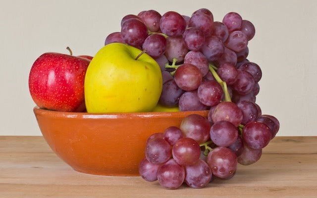 Purple grapes in a bowl with one red apple and one yellow apple