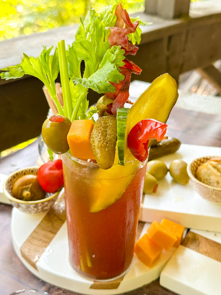 a Bloody Mary Cocktail with garnish of celery, bacon, dill pickle, and a skewer of olives, cheese, pickles.