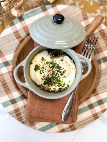 country breakfast topped with egg and parsley in a mini baker styled on a plaid charger.