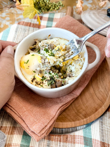 a hand holding a breakfast mini bake at a table while the other hand holds a fork full of the breakfast food up toward the camera.