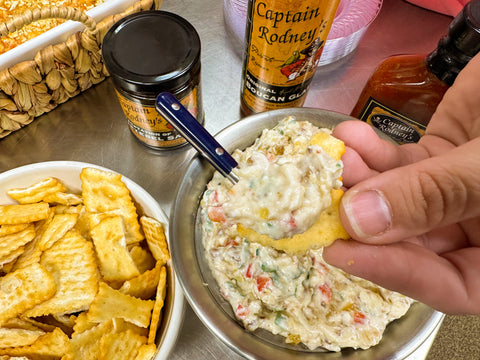 a bowl of Captain Rodney's Tempation of Jezebel Dip next to a bowl of crackers. A hand holds a cracker full of the dip up to the camera.