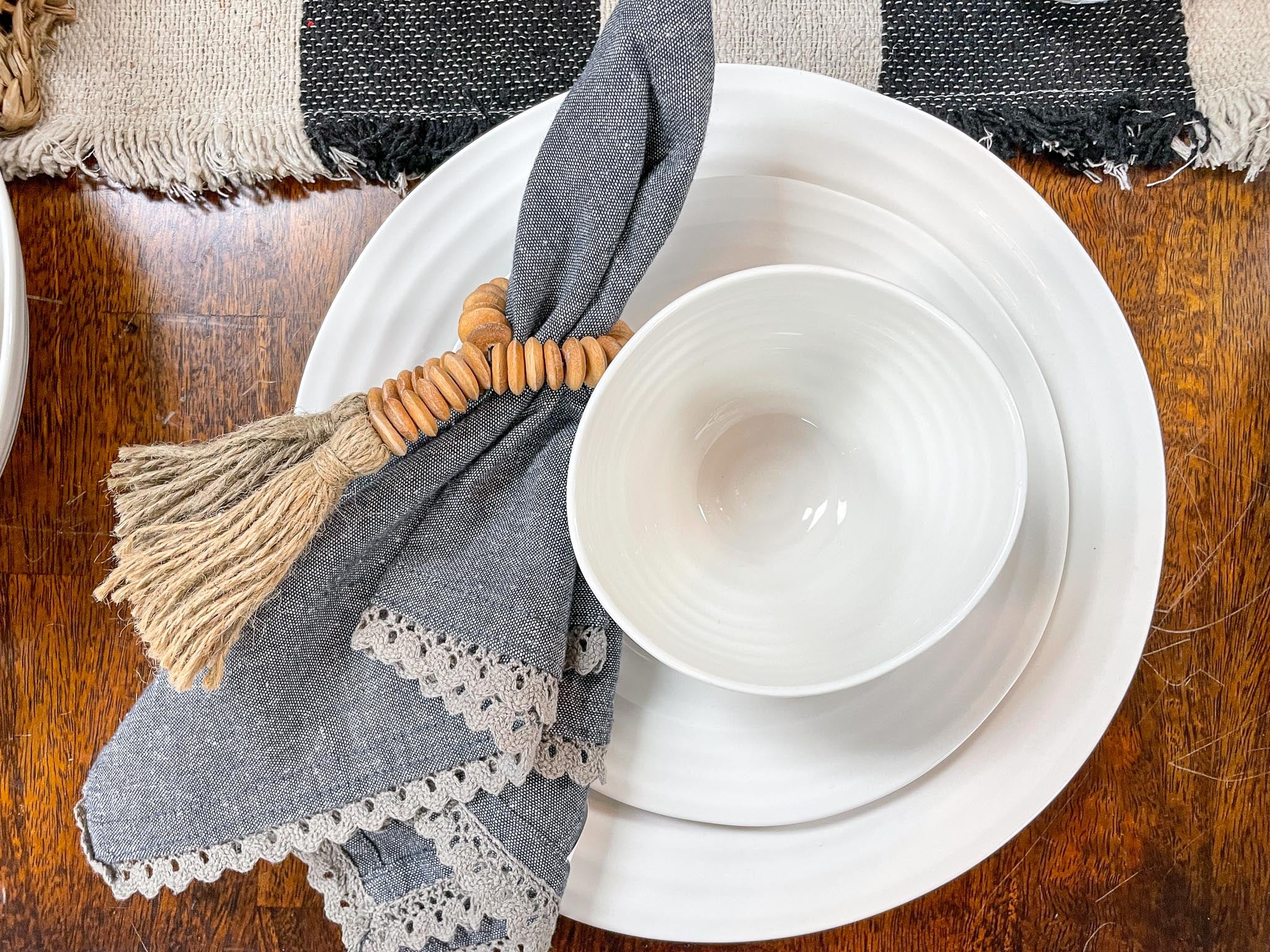 Sophie Conran white dishes stacked with a blue napkin on a brown tabletop.