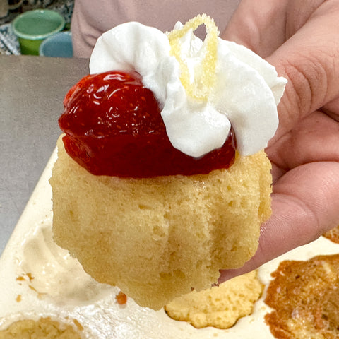 mini lemon bundt cake with strawberries and whipped cream topped with candied lemon peel.