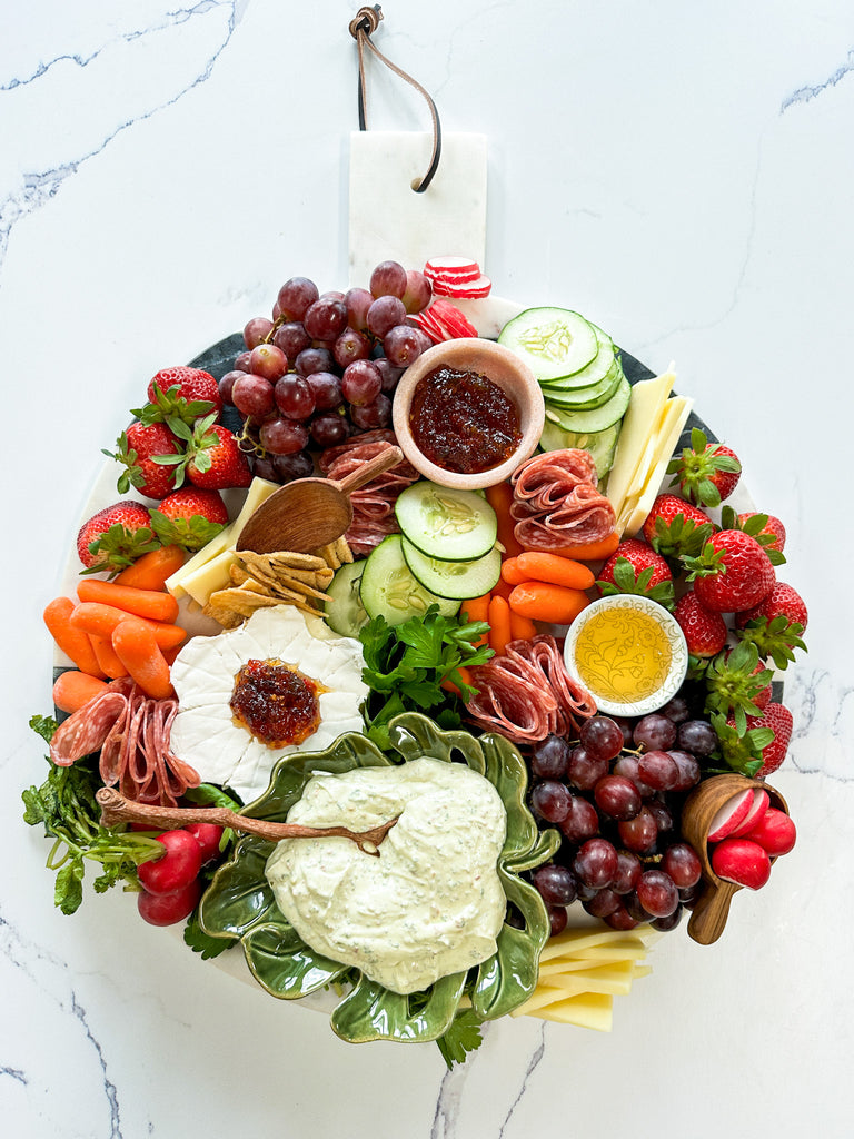 round marble charcuterie board filled with dips, honey, cheese, and fresh vegetables