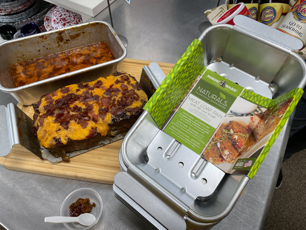 a stack of nordicware meat loaf pans sits alongside a baked meatloaf atop a wooden cutting board