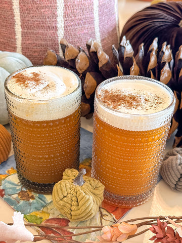 two glasses of pumpkin pie cider fizz topped with toasted marshmallow whipped cream sit on a paper napkin with a corduroy pumpkin and faux leaves