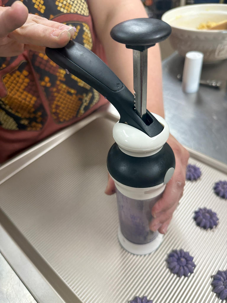 oxo cookie press pressing cookies on a baking sheet.