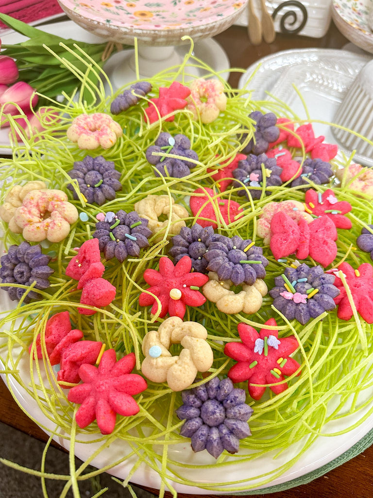 plate of colored butter cookies in flower and butterfly shapes on a bed of edible Easter grass. 