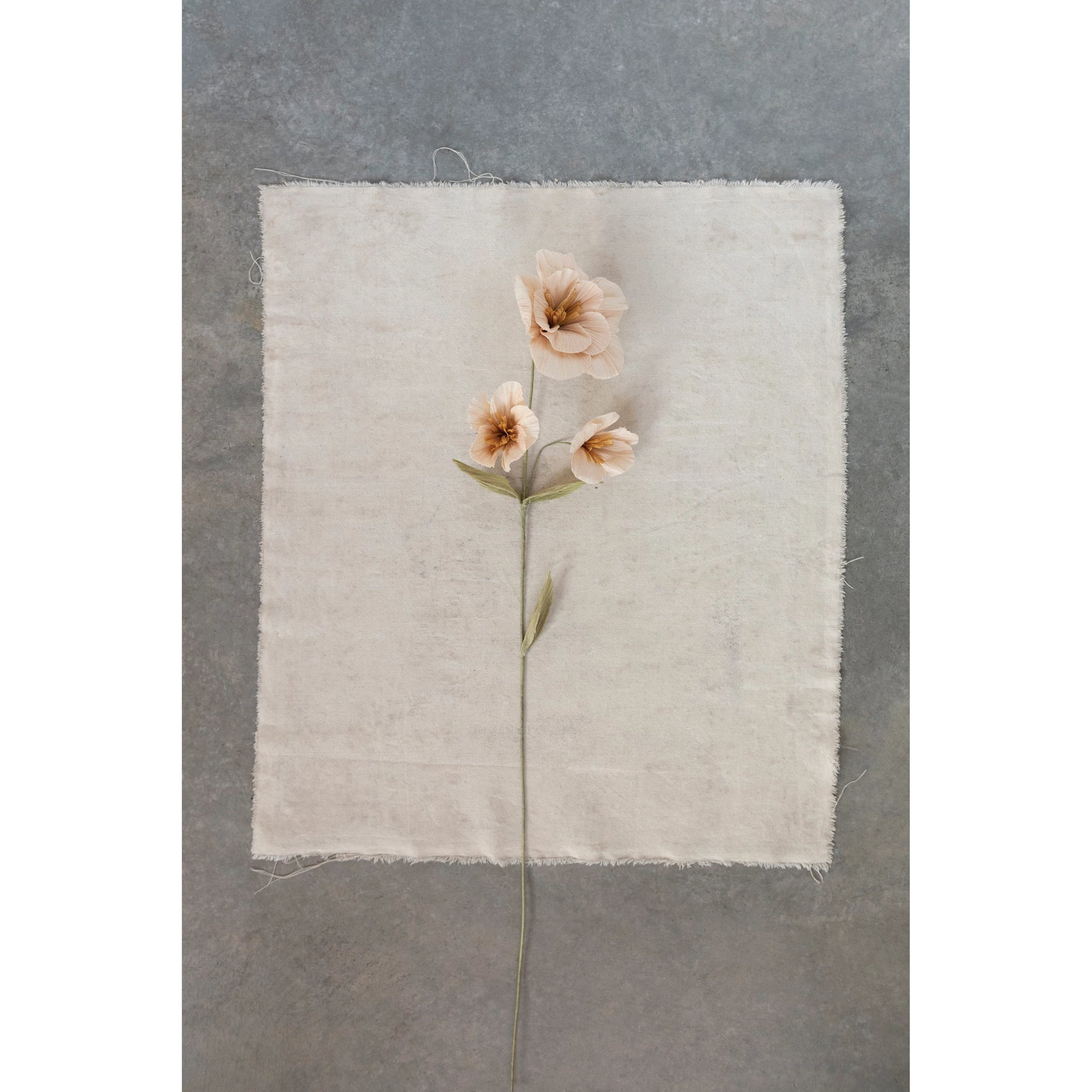 stem with 3 blush flowers laying on a piece of natural linen.