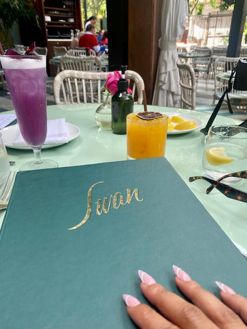 Manicured hand placed on a menu with two cocktails in background of restaurant