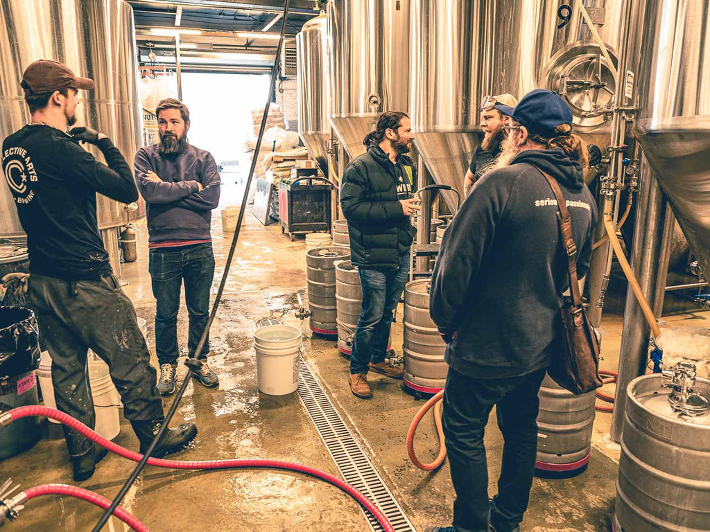 The Hawkers crew and Other Half crew standing and talking among brewery tanks at Other Half