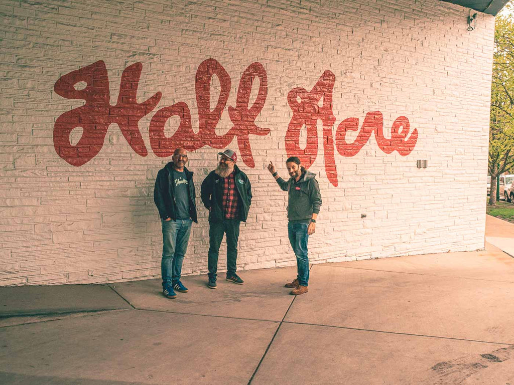 Maz, Alex and Tony standing in front of Half Acre logo on brick wall outside the brewery