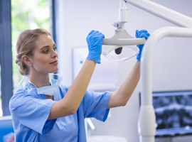 female nurse adjusting medical equipment wearing blue scrubs and blue rubber gloves