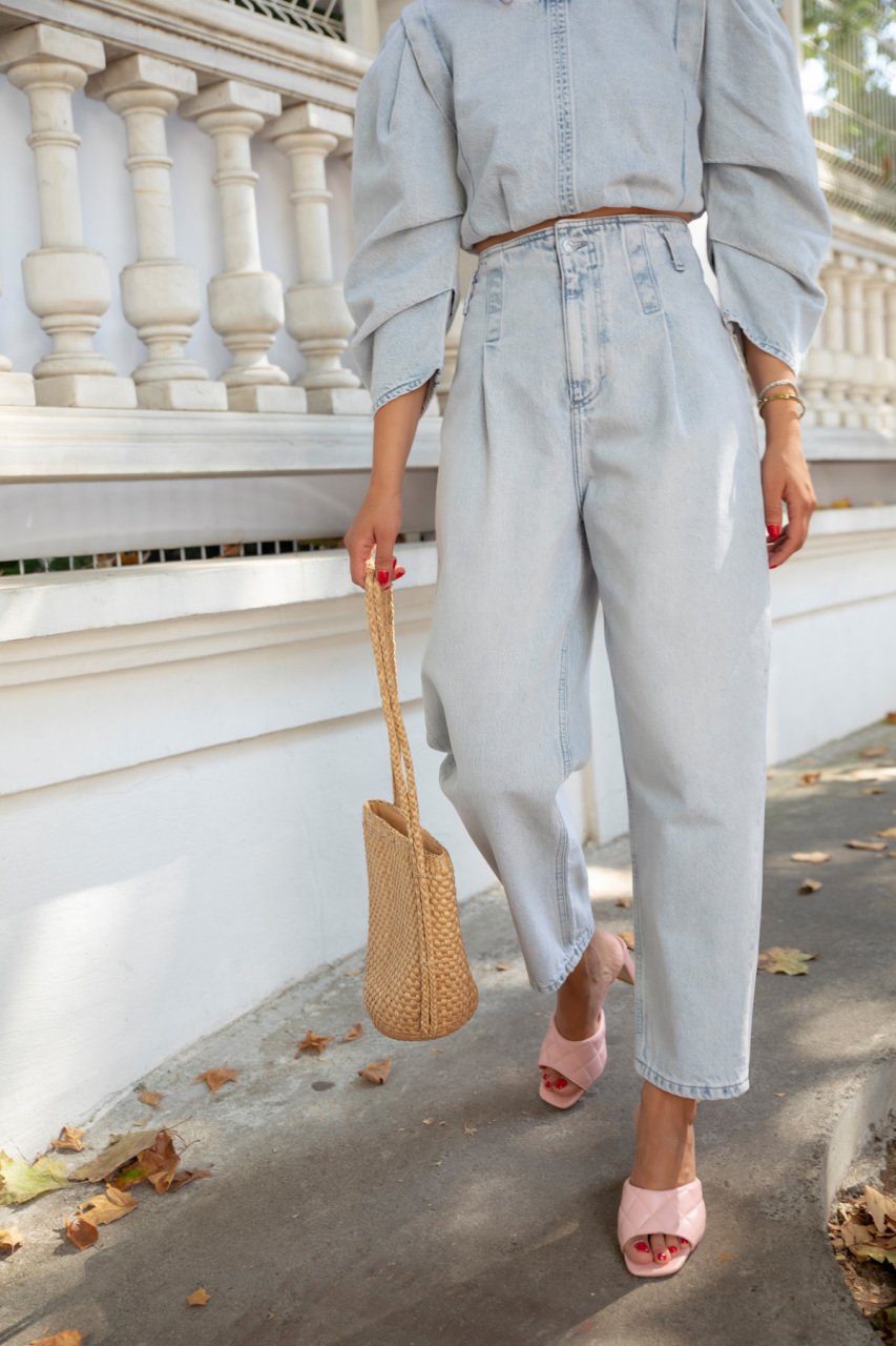 Image of Bynes New York Apparel & Accessories Streewear Highwaist Jeans. Jeans are depicted on a model walking down the street wearing pink open toed heels and carrying a straw look bag. 