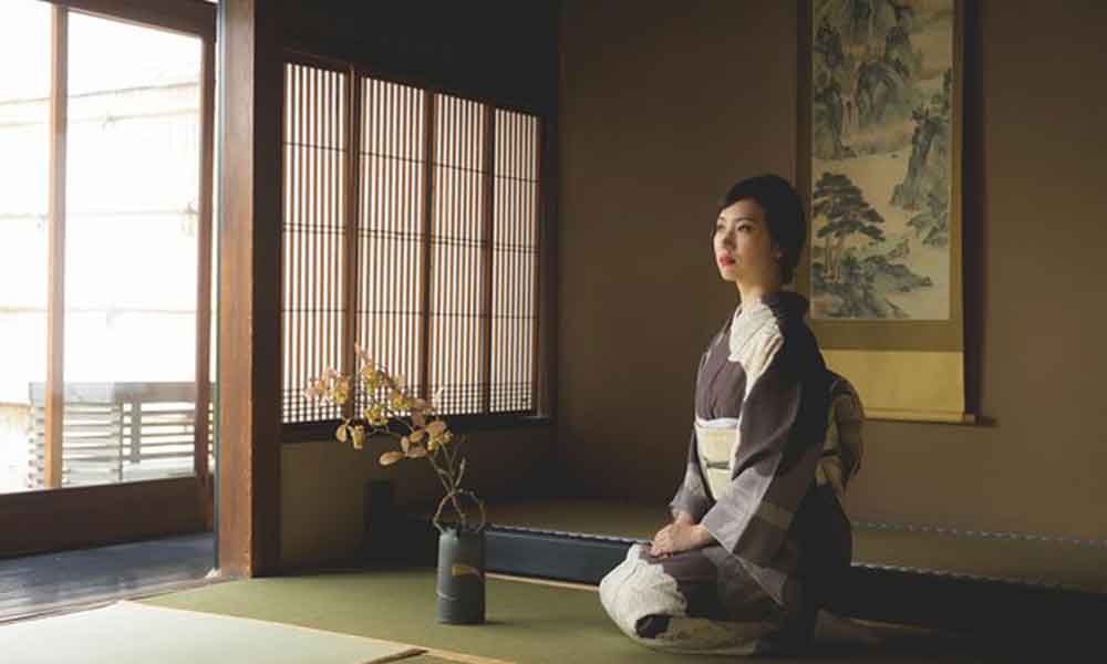 Une femme en kimono est assise et comtemple la decoration maison japonaise avec un vase ikebana