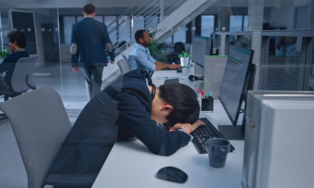 Un homme fait une sieste au travail japon sur son bureau à côté de ses collègues: inemuri. La sieste japonaise en public