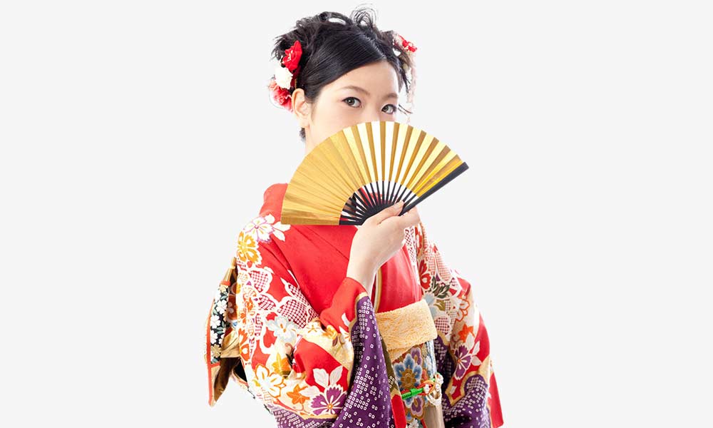 Quelle est la signification éventail japonais quand il est ouvert? Une femme geisha est habillée avec un kimono rouge et se cache le visage derrière son éventail Sensu