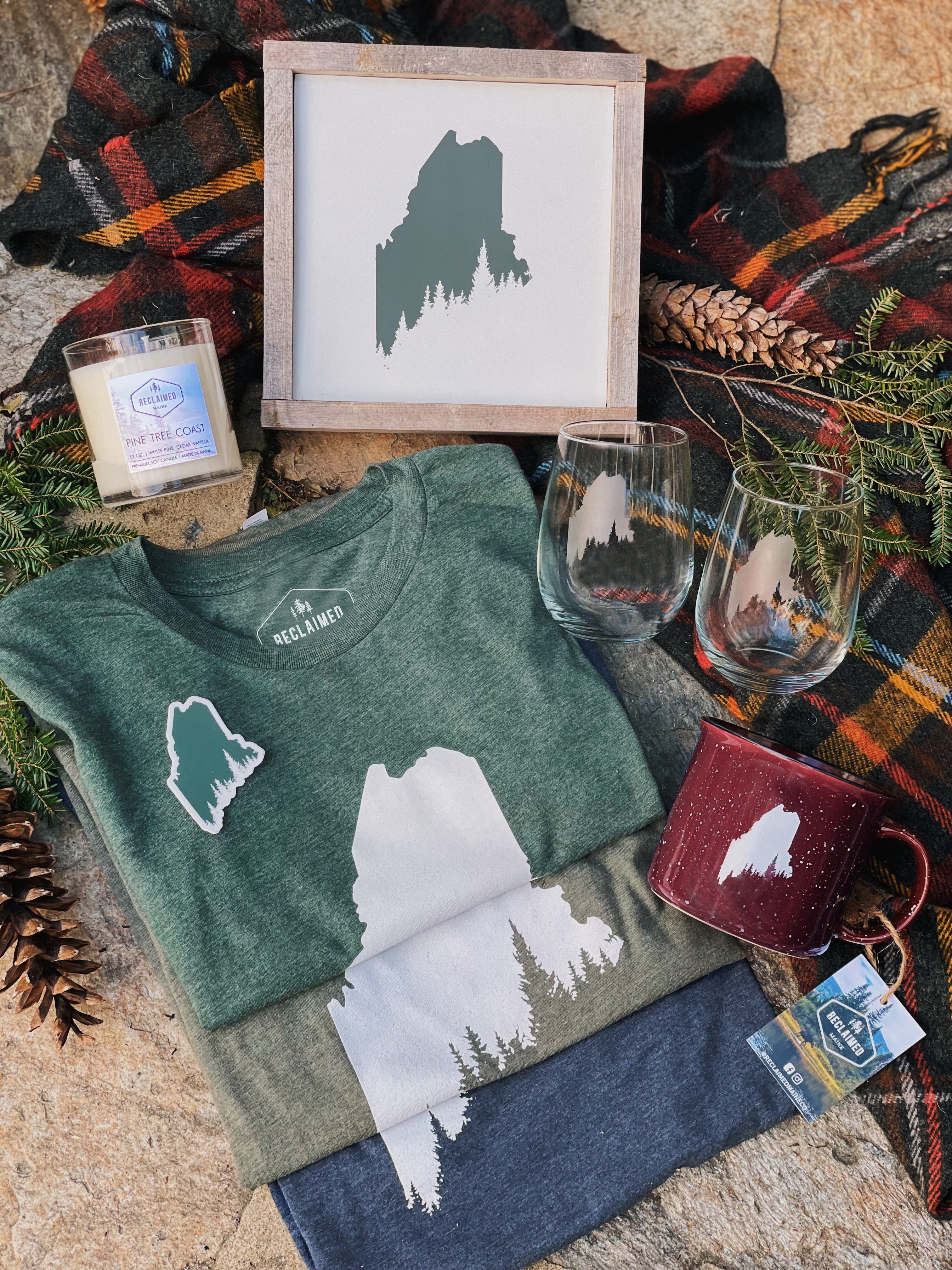 collection of tshirts, wood signs, glasses, mugs and candle with Maine pine tree coast design