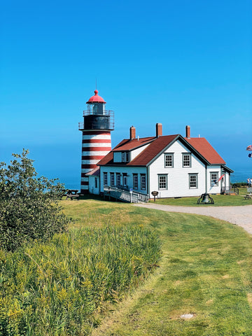 red and white striped lighthouse, with green grass and bright blue sky