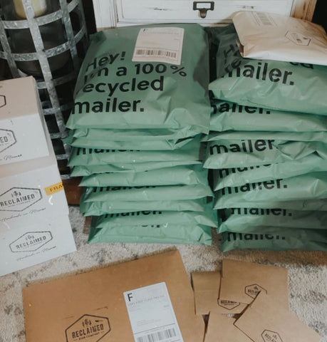 stack of green 100% recycled poly mailers with kraft mailers in front and white boxes