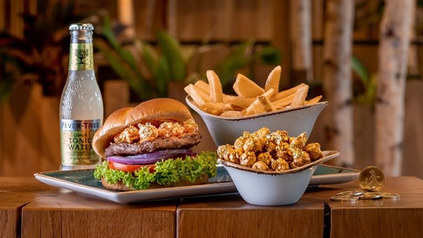 A beef burger topped with the signature Hans Im Glück sauce featuring The Kettle Gourmet’s Kaya Butter Toast popcorn, garnished with edible gold flakes and accompanied with potato wedges and tonic water