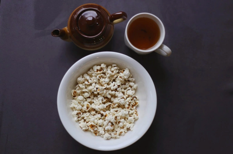 a pot of tea with a cup filled with it to pair with the popcorn