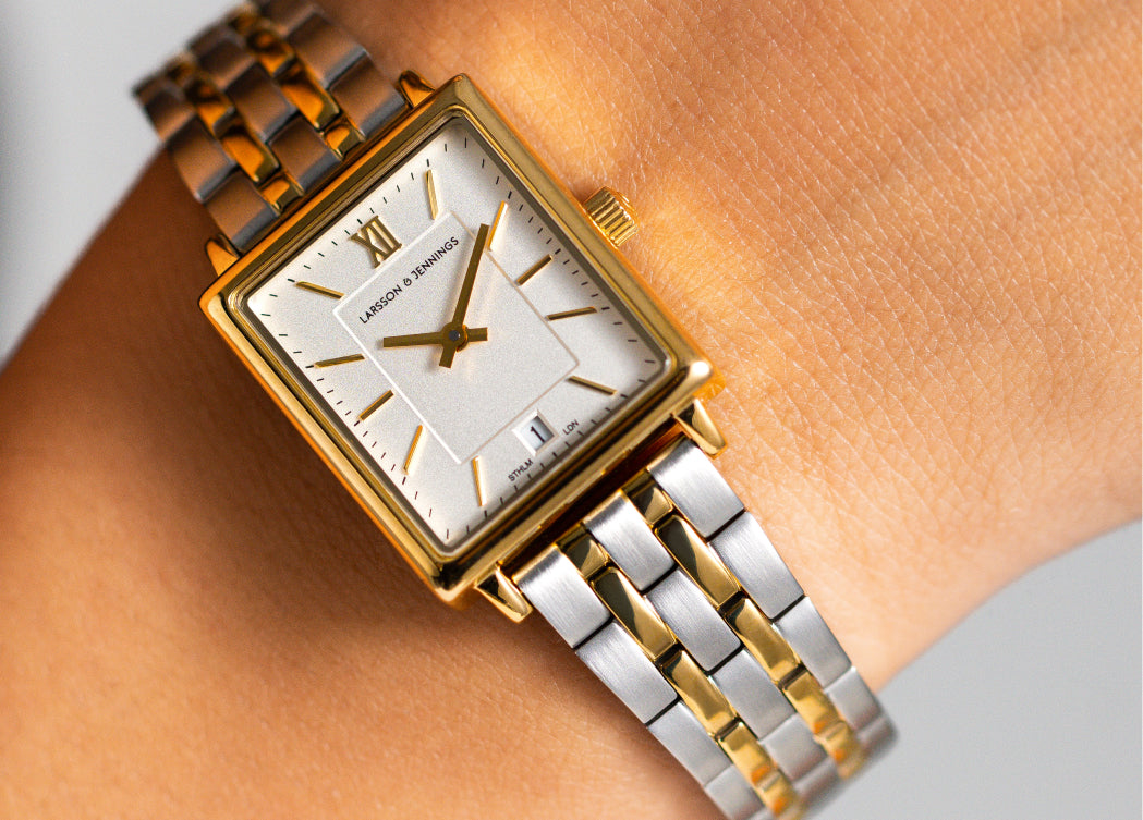 Rectangular silver and gold watch with a metal band worn on a wrist.