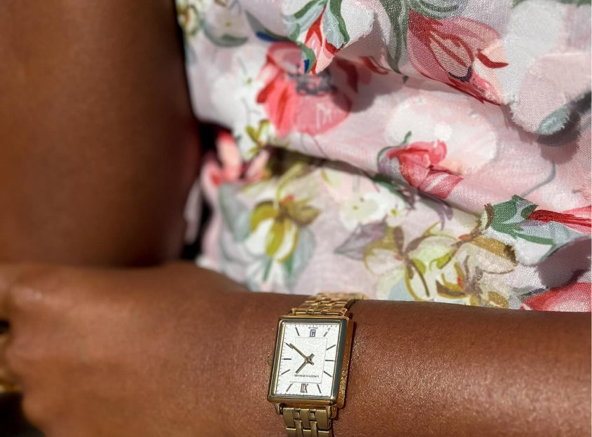 A close-up of a person wearing a gold wristwatch and a floral-patterned shirt.