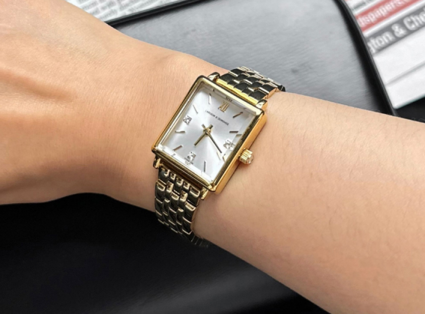 A wrist wearing a classic rectangular gold watch with a white face and metallic strap.