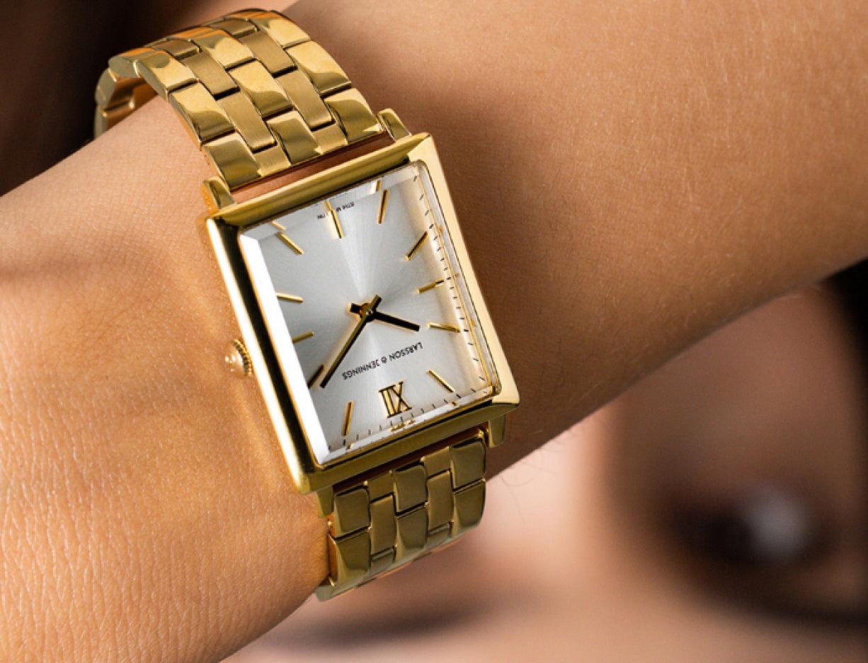 Close-up of a gold wristwatch with a rectangular face on a person's wrist.