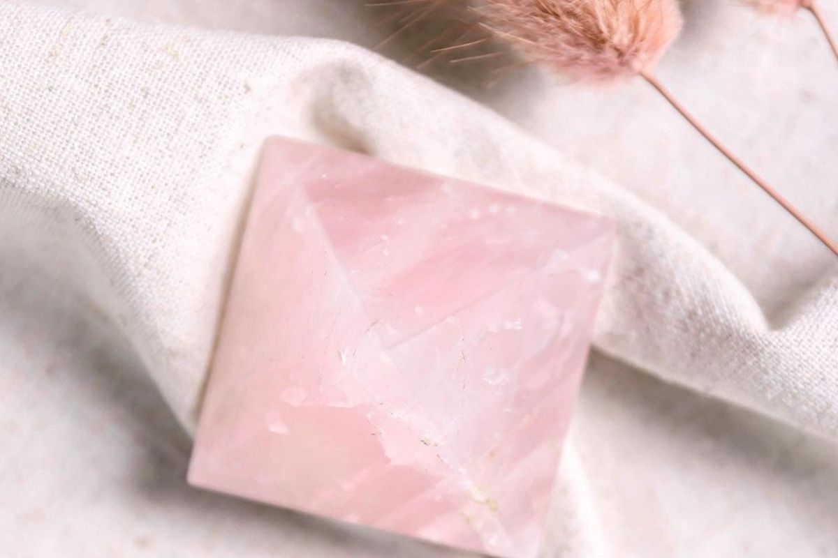rose quartz pyramid against linen and pink feather