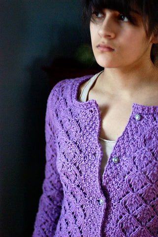 Brunette model wearing a purple lacy jewel-neck cardigan sweater unbuttoned at the neck.