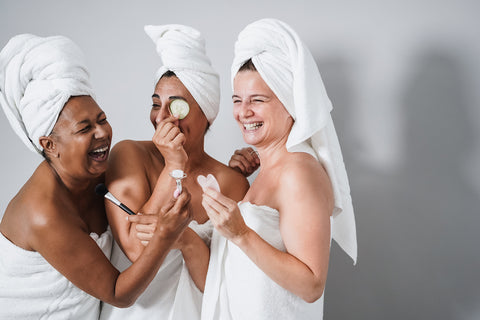 three women laughing and putting on skincare