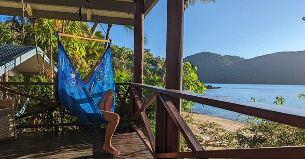 Some sitting in a hammock chair on a deck looking out at the beach