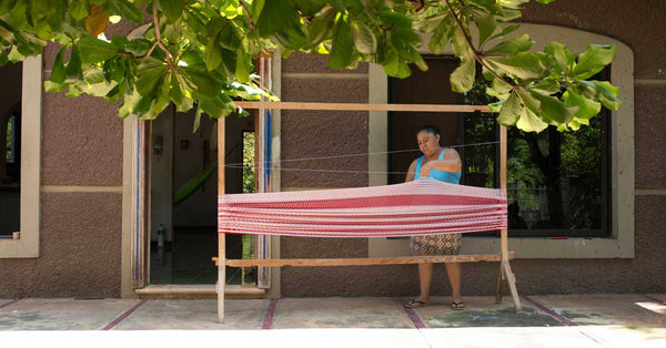 A mayan woman weaving a hammock on a loom on her front porch