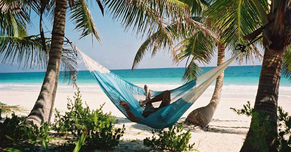 A guy relaxing in a mayan hammock between two palm trees on the beach.