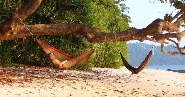 A guy relaxing on the beach in a nylon camping hammock