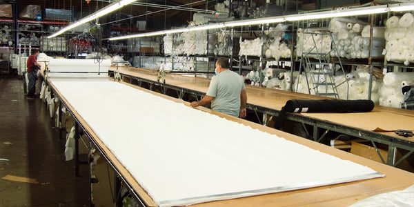 worker rolling out a large roll of white fabric onto a cutting table