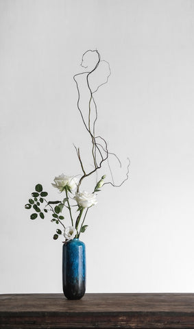 Two white flowers and log twigs in a blue vase