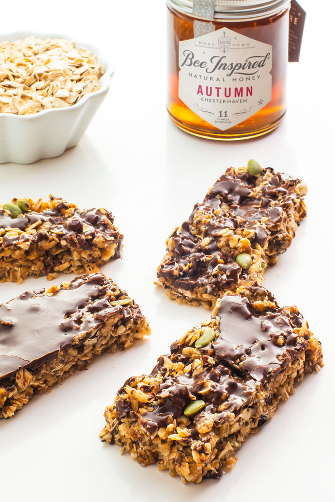 peanut butter honey granola bars sit in front of a bowl of oats and a jar of honey