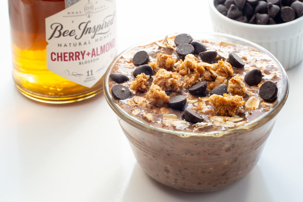 a bowl of overnight oats with chocolate chips sits on a table in front of a jar of honey